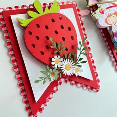 a close up of a card with a strawberry on it and flowers in the middle