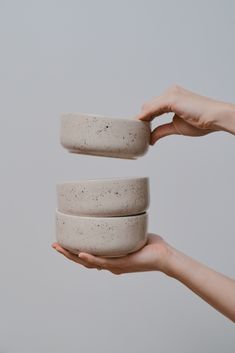 two hands are holding small bowls in front of each other, one is white and the other is gray