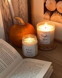 an open book sitting on top of a wooden table next to candles and pumpkins