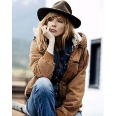 a woman wearing a brown jacket and black hat sitting on a rail talking on her cell phone