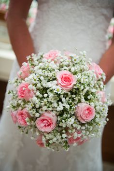 a bride holding a bouquet of pink roses and baby's breath in her hands