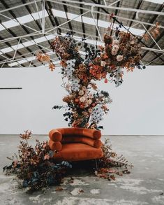 an orange chair sitting in front of a floral arrangement on top of a white wall