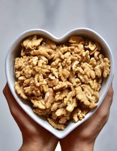 a heart - shaped bowl filled with walnuts in someone's hands on a white background