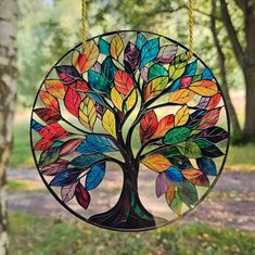 a stained glass tree ornament hanging from a rope in a park with trees