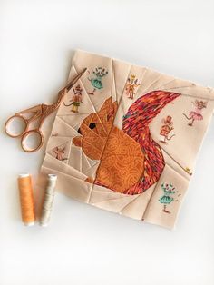 scissors and thread are sitting on top of a piece of fabric with a squirrel design