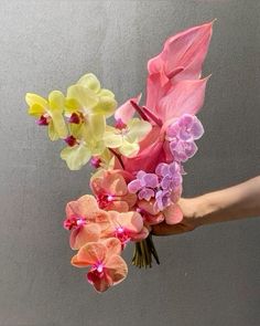 a hand holding a bouquet of flowers with pink and yellow orchids in it's center