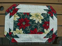 a close up of a quilted table topper on a wooden bench with poinsettis