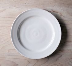 an empty white plate sitting on top of a wooden table next to a knife and fork