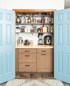 a kitchen with blue doors opened to reveal the pantry and coffee maker on the counter