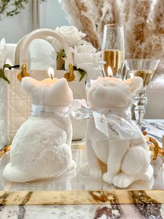 two white teddy bears sitting next to each other on a table with champagne and flowers in the background