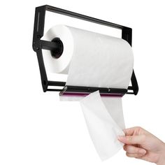 a hand holding a roll of toilet paper in front of a black holder with two rolls on it