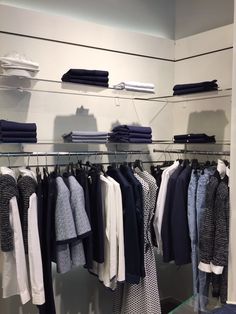 clothes are hanging on racks in a clothing store, with folded shirts and sweaters