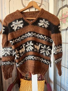 This super soft sweater was made by hand from a wool blend in medium brown and black, accented by various designs in light beige. The measurements, taken with the sweater lying flat, are: shoulder to shoulder, 18 inches; armpit to armpit, 20 inches; sleeves, 22 inches; length, 20 inches; bottom edge, 13 inches (with stretchy ribbing). In very good condition. Brown Knit V-neck Sweater For Winter, Brown Knitted V-neck Sweater, Cozy Brown Knit V-neck Sweater, Brown Nordic Sweater For Fall, Winter Brown Alpaca Sweater, Brown Fair Isle Pattern Winter Sweater, Brown Fair Isle Winter Sweater, Nordic Brown Knit Sweater, Brown Nordic Knit Sweater