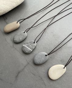 Handmade beach stone necklace , the sea pebble have been hand drilled and threaded onto a extra strong silk string, the end of string have a gray colour gemstone each side.  Pendant size:  Style 1: 1.2cm x 3.5cm Style 2: 1.8cm x 3.0cm Style 3: 2.1cm x 3cm Style 4: 1.9cm x 2.8cm Style 5: 2cm x 3.2cm A 2.4 x 3.5cm B 2 x 3.2cm C 2.2 x 3.6cm D 2.5 x 3.4cm E 1.8 x 3.5cm F 1.8 x 3.8cm G 1.6 x 4cm H 2 x 3cm I 2 x 3cm J 1.8 x 3.6cm the necklace is adjustable can be worn long and short, one size to fits all. The shape and colour of stone are completely natural, each piece is one of a kind. A Great natural gift for all ages. Beach Stones Jewelry, Pebble Jewelry, Pebble Pendant, Pebble Necklace, J 1, Stone Ornaments, Stone Art Painting, Rock Necklace, Stone Jewellery