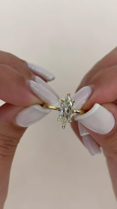 a woman's hands with white and gold nail polish holding a diamond shaped ring