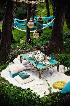 an outdoor picnic with hammocks and pillows on the ground in front of trees