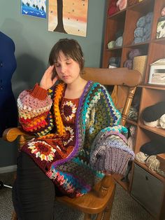 a woman sitting in a rocking chair with a crocheted blanket on her shoulders