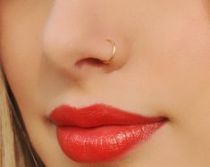 a close up shot of a woman with red lipstick and gold nose ring on her nose