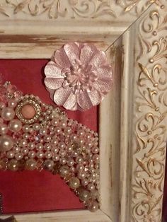 a white frame with pearls and a pink flower on it in front of a red wall