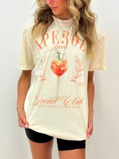 Indulge in your dreams of an Italian summer with our best selling Aperol Spritz Cocktail Club tee! With its sleek design and comfortable fit, this shirt is perfect for any cocktail lover. Show off your passion for your favorite drink in style and make a statement with this must-have shirt.  100% pre-shrunk cotton!  Professionally direct to garment printed on ivory Comfort Colors apparel. No transfers and no vinyl means no cracking! :)  Tees are true to size for a relaxed, slightly boxy unisex fi Summer Brunch T-shirt With Screen Print, Summer Crew Neck Top For Brunch, Spring Brunch Graphic Print T-shirt, Summer Graphic Tee For Brunch, Summer Graphic Print T-shirt For Brunch, Spring Graphic Print T-shirt For Brunch, Trendy Summer T-shirt For Brunch, Summer Cotton Shirt For Brunch, Trendy Relaxed Fit T-shirt For Brunch