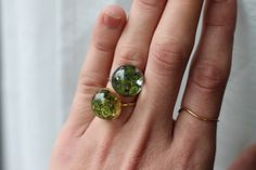 a woman's hand holding two rings with green and yellow stones on them,