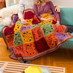 two people sitting on a couch with a crocheted blanket in the shape of squares