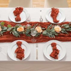 the table is set with white plates and red napkins, silverware and flowers