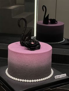 two cakes decorated with black swan decorations on top of each other, one is pink and the other is purple