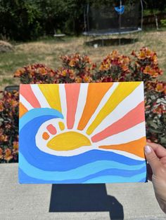 a hand holding up a piece of art that looks like the sun is rising over water