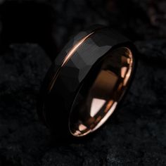 a black and rose gold wedding ring on top of a stone surface with the light shining through it