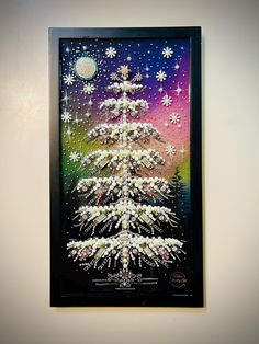 a christmas tree with snowflakes on it in a black frame hanging on the wall