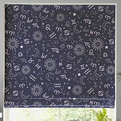 a window with roman blinds decorated with zodiac signs and stars on it, in front of a potted plant