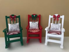 three miniature chairs with pillows and bows on them, sitting side by side in front of a wall