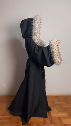 a person in a black robe with fur on their head and arms, holding something up to the side