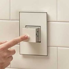 a person is pressing the button on a wall light switch in a white tiled bathroom