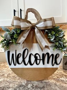 a welcome sign hanging from the side of a kitchen counter with greenery on it