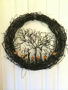 a wreath with branches and pumpkins hanging on the front door