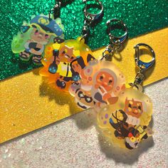 two keychains with cartoon characters on them sitting next to a yellow and green glitter background