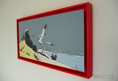 a red frame hanging on the wall above a painting with seagulls flying over it