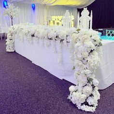 a table with white flowers on it in front of a blue lit up stage at a wedding