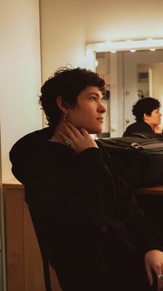 a woman sitting in front of a mirror with her hand on her neck