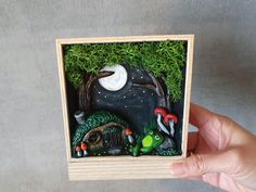 a hand holding a small wooden box with an image of a forest scene in it