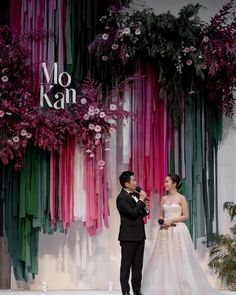 a man and woman standing next to each other in front of a wall with flowers