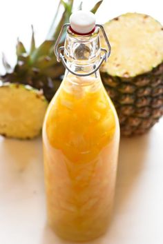 a pineapple juice in a glass bottle next to some cut up pineapples