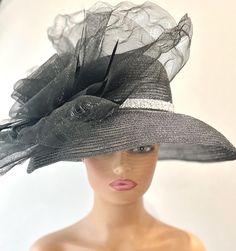 The featured hat is a very dramatic and gorgeous black straw mesh hat with some silver metallic threading running through the whole hat giving the black hat a bit of sparkle. The hat has a curved downward turned brim. A sparkly band with encrusted silver beads goes around the base of the hat. The hat is adorned with a very very large black crinoline disc with a center flower and accent black feathers. This hat is so dramatic and gorgeous and the good news is that there was only one hat made in t Black Cloche Party Hat, Black High Crown Hat For Summer, Black High Crown Hat For Evening, Black Top Hat With Wide Brim For Evening, Black Wide Brim Fascinator For Evening, Black Wide Brim Costume Hat For Evening Events, Black Wide Brim Costume Hat For Evening, Black Evening Top Hat With Wide Brim, Black High Crown Costume Hats And Headpieces For Wedding