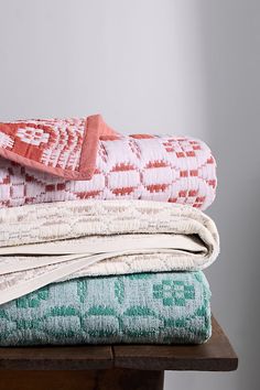 folded towels stacked on top of each other on a wooden table in front of a gray wall