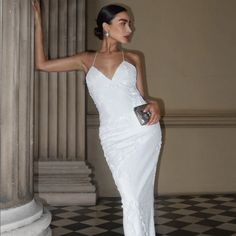 a woman in a white dress standing next to a pillar and holding a clutch bag