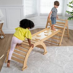 two children playing on a wooden bench in a room with white walls and hardwood floors