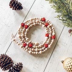 beads and pine cones are arranged on a white wooden surface with evergreen branches, pine cones, and other holiday decorations