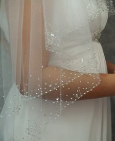 a woman in a wedding dress is wearing a veil with pearls on it and holding a cell phone